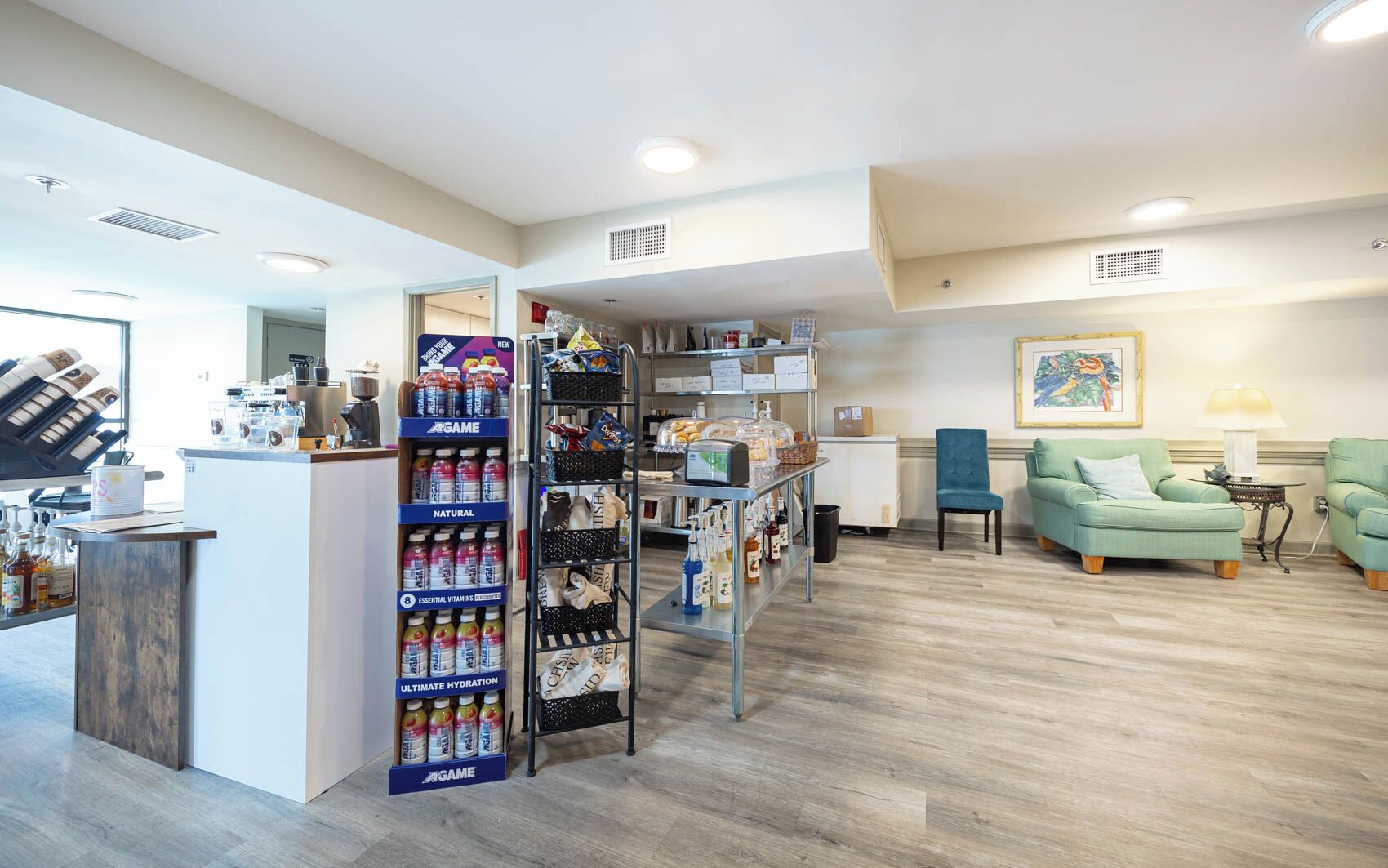 A modern interior with a reception desk, a beverage display, a seating area with a green sofa, and a wooden floor.