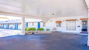 A motel with a covered parking area, individual rooms with blue doors, and a small outdoor seating area. - American Inn by OYO Colorado City I-20 (Colorado City)
