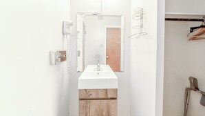 A bathroom with a white sink, mirror, and light fixture. There is a wooden cabinet below the sink and a door with a mirror above it. - American Inn by OYO Colorado City I-20 (Colorado City)