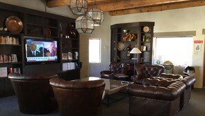 A cozy living room with leather sofas, a coffee table, and a television displaying news.