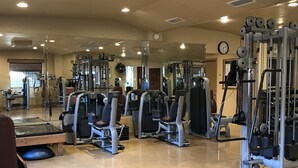A gym with various exercise machines, a mirrored wall, and a clock on the wall.