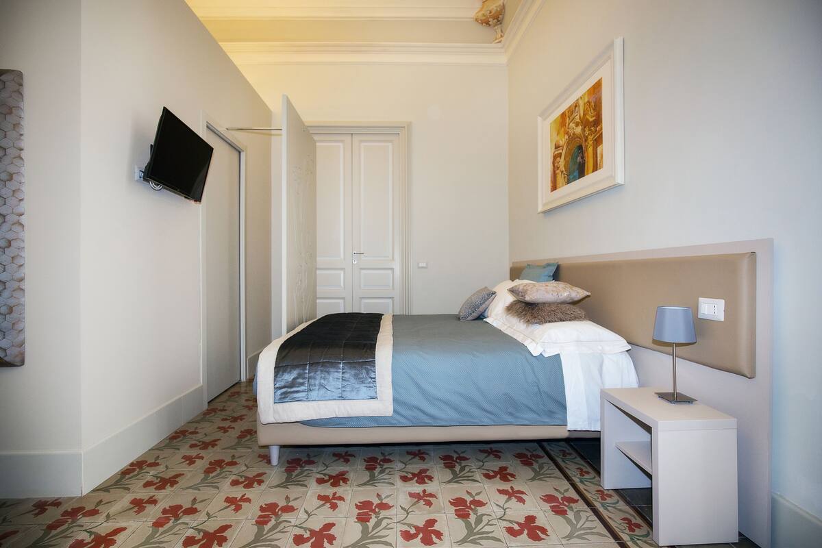 Un dormitorio con cama, mesita de noche y televisor en la pared.