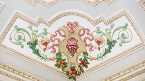 Een plafond met decoratieve bloem- en fruitmotieven, gouden afwerking en een centraal medaillon.
