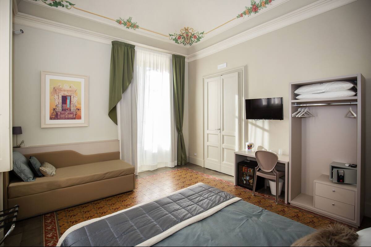 Habitación de hotel con cama, escritorio, silla, televisor, armario y sofá.