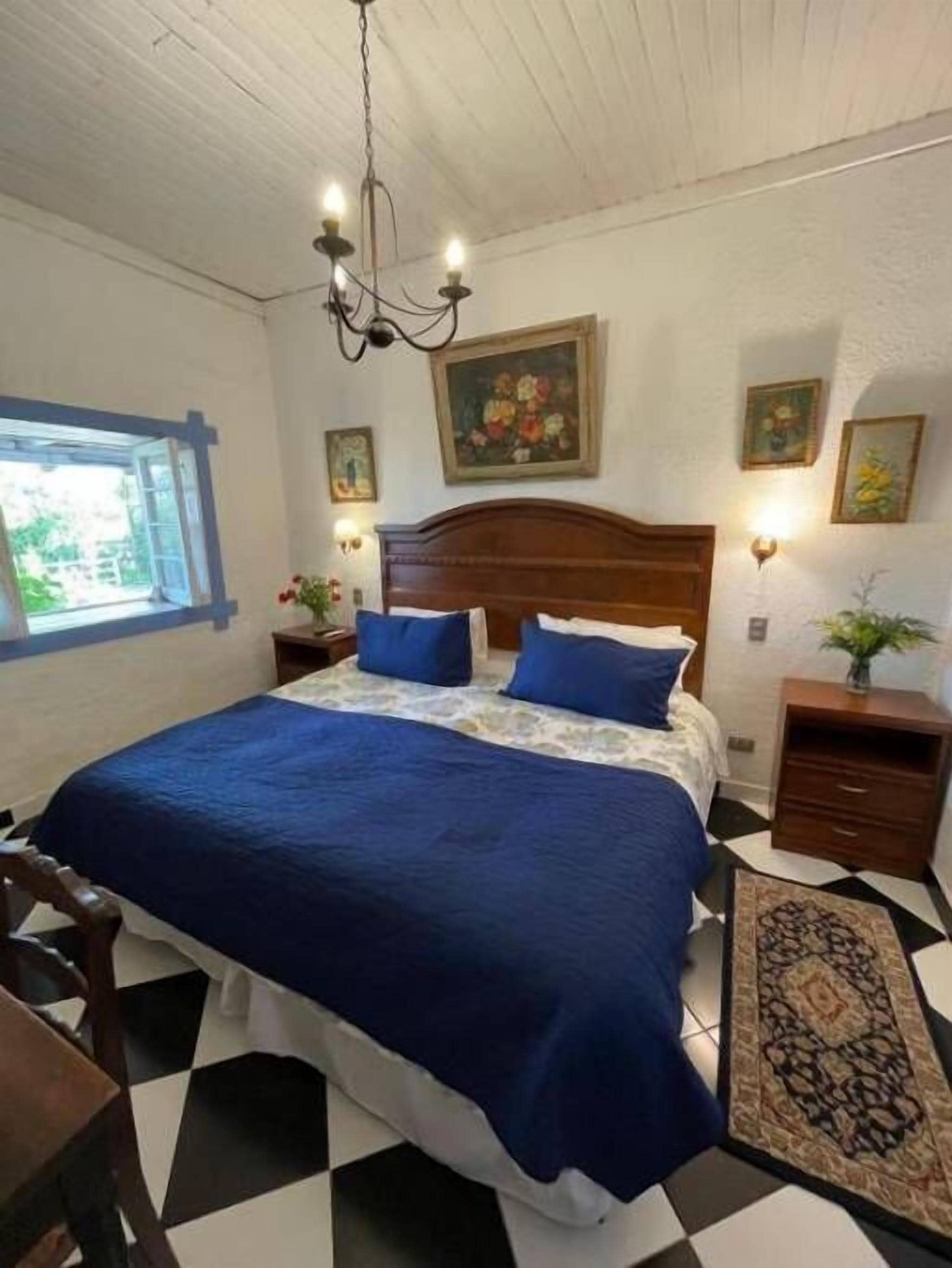 Quarto com cama grande, cabeceira de madeira, janela com vista e lustre.