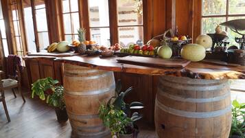 Balcão de madeira com frutas, legumes, barris de madeira e plantas em vasos em ambiente rústico.