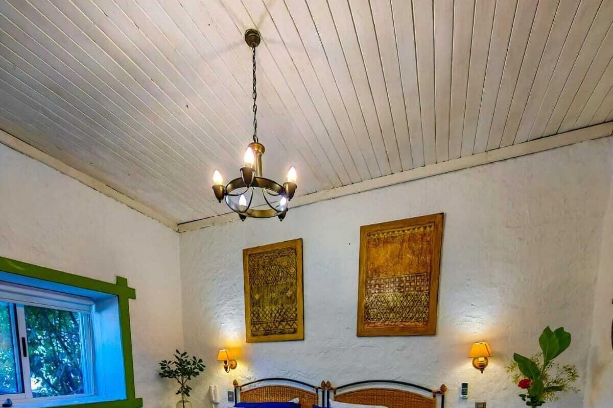 A room with a checkered floor, a bed with a blue bedspread, a chandelier, and two wall-mounted lamps.