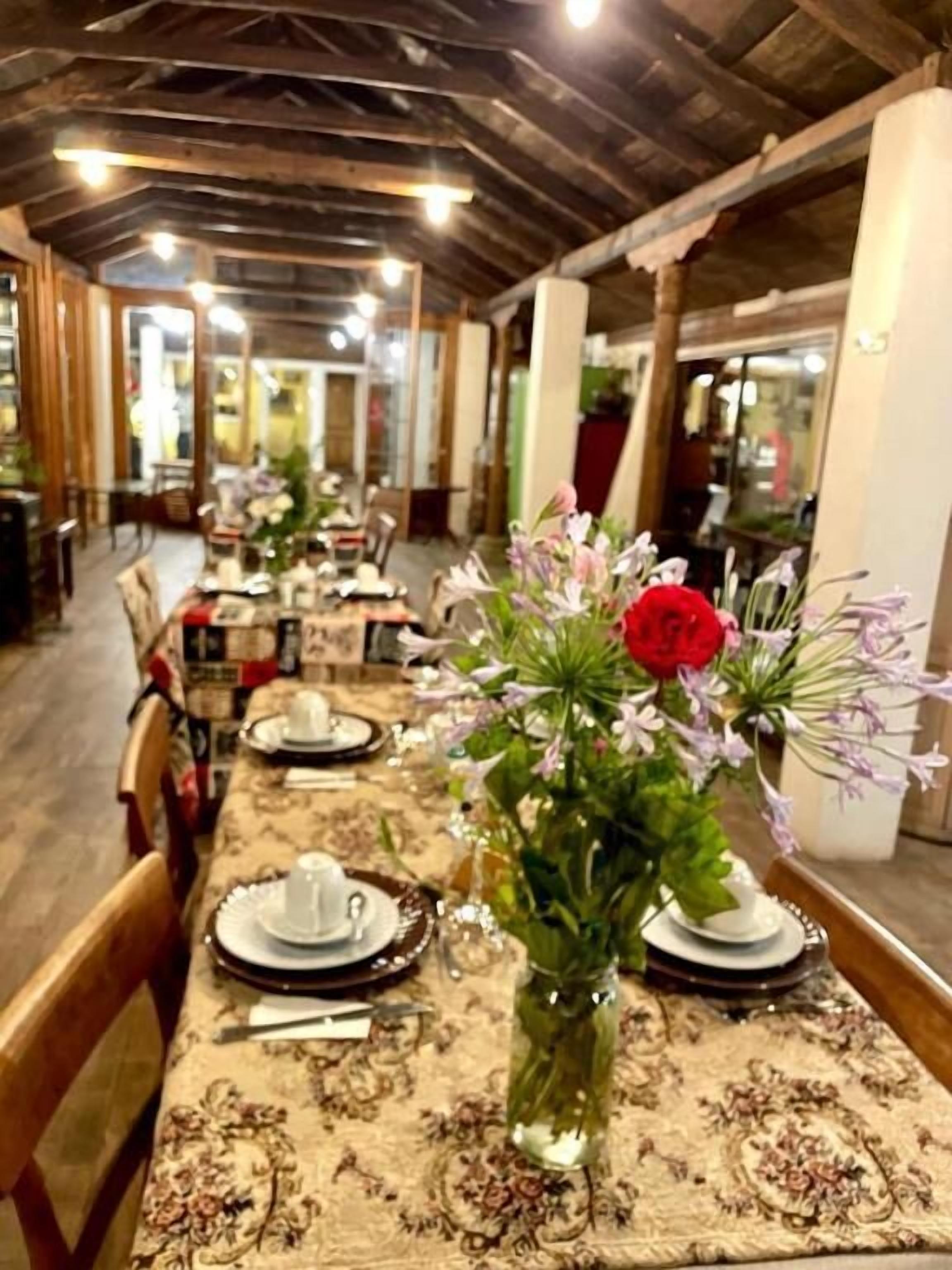 Uma longa mesa de jantar com centros de mesa florais, posta para uma refeição.