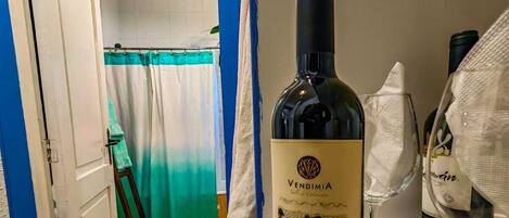 A room with a wine bottle and glass on a counter, a door leading to a bathroom, and a hanging light fixture.