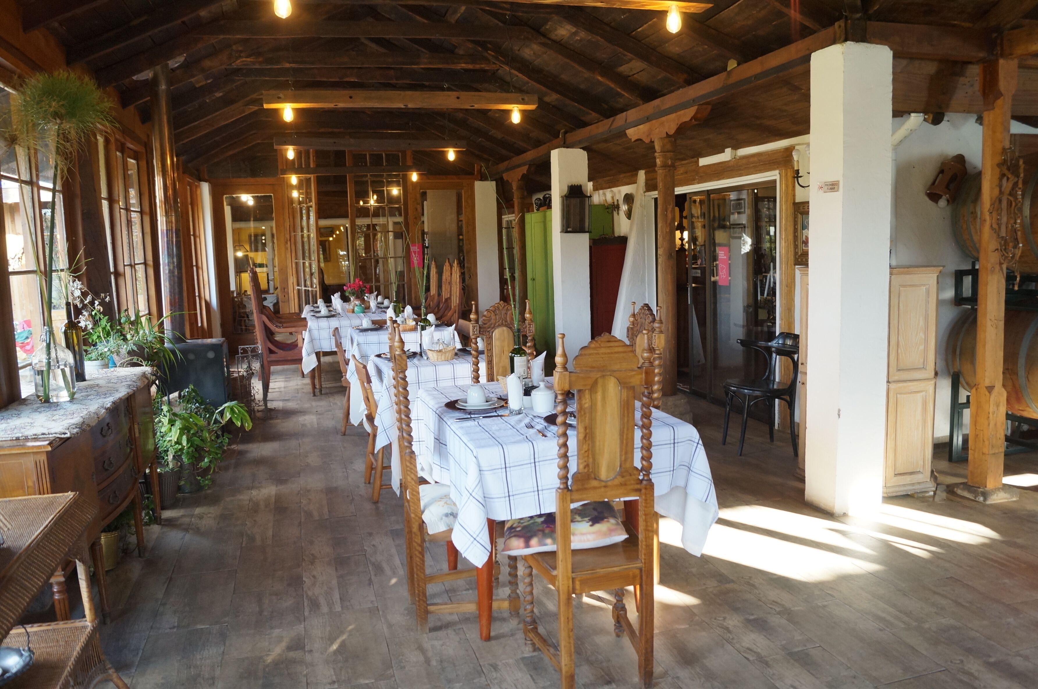 A rustic dining area with wooden tables and chairs, a wooden floor, and large windows allowing natural light.