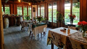 A rustic dining area with wooden tables and chairs, large windows, and potted plants. - Hotel Vendimia Parador (Santa Cruz)