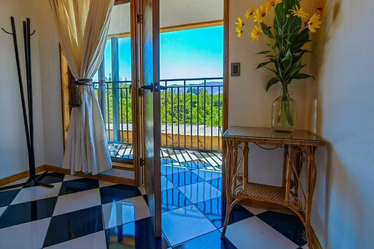 A room with a checkered floor, a balcony with a view, and a vase with flowers.
