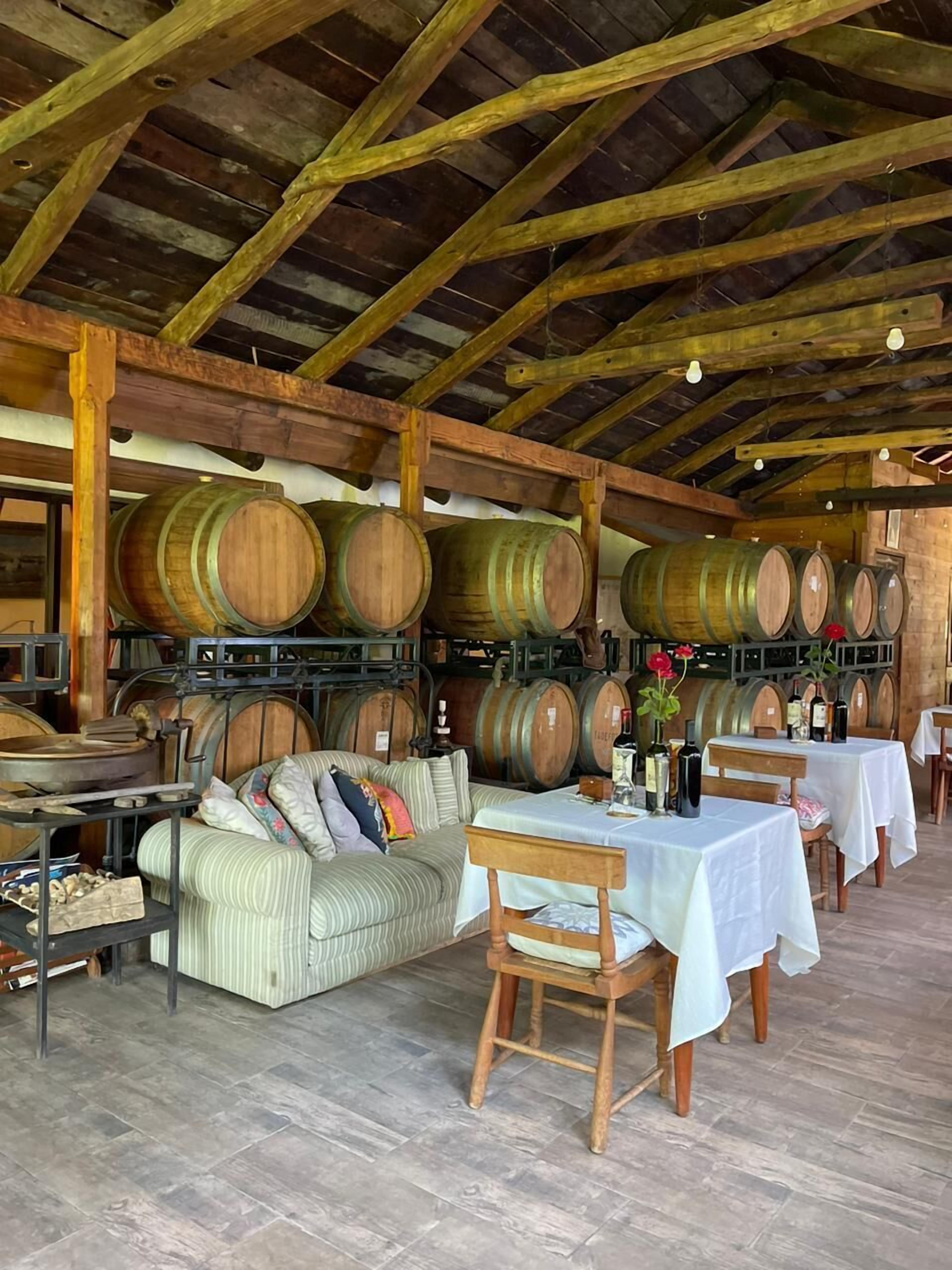 Un interior rústico con barriles de madera, un sofá y mesas dispuestas para comer.