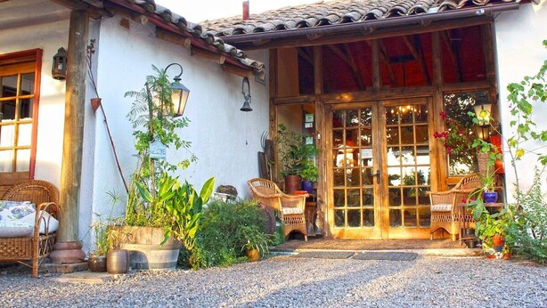 A traditional building with a tiled roof, a welcoming sign, and a large glass door. - Hotel Vendimia Parador (Santa Cruz)