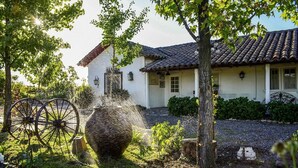 A traditional house with a tiled roof, a garden with a large pot and a wheelbarrow, and a well-maintained lawn. - Hotel Vendimia Parador (Santa Cruz)