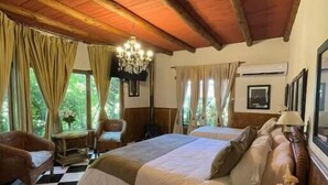 A cozy bedroom with a large bed, two chairs, a small table, and a chandelier. - Hotel Vendimia Parador (Santa Cruz)