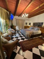 Una habitación de hotel con piso a cuadros, cama con colcha estampada, candelabro, televisión y muebles de mimbre.