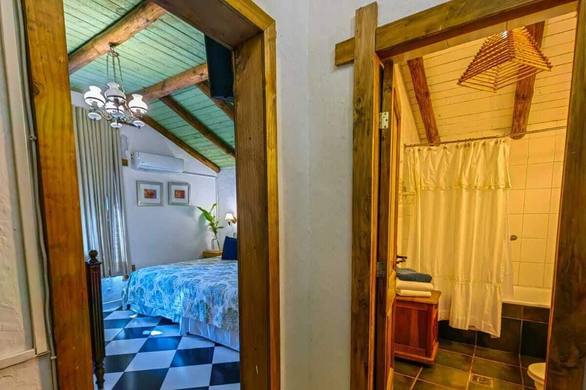 A room with a checkered floor, a bed with a blue patterned bedspread, a wooden door, and a small wooden cabinet.
