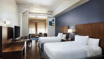 A hotel room with two beds, a desk, a chair, a lamp, and a painting on the wall.