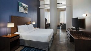 A hotel room with a large bed, a desk with a TV, a painting on the wall, and a view of the hallway. - Fairfield Inn & Suites by Marriott Dallas Downtown (Dallas)