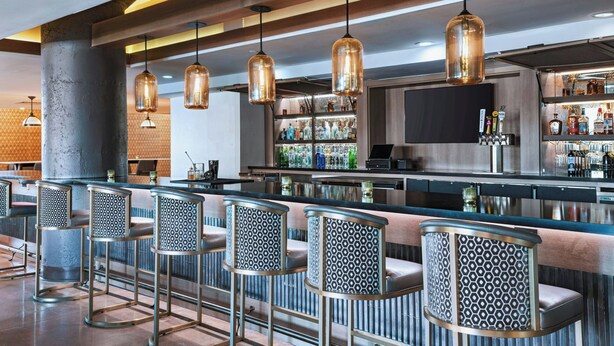 A bar area with a long counter, multiple stools, hanging pendant lights, and a variety of bottles on shelves. - Fairfield Inn & Suites by Marriott Dallas Downtown (Dallas)