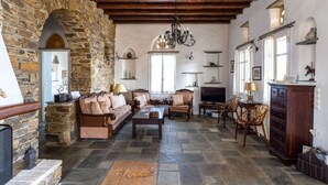 A cozy living room with stone walls, wooden beams, and a fireplace. There are comfortable sofas, a coffee table, and a TV. - Maison Simone, a great escape experience!! (Αγ. Σώστης)