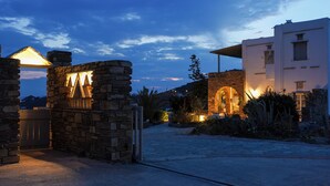 A stone archway leading to a building with a lit-up entrance, surrounded by a landscaped garden and a clear sky. - Maison Simone, a great escape experience!! (Αγ. Σώστης)