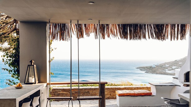 A patio with a swing, a table, and chairs overlooking the ocean. - Maison Simone, a great escape experience!! (Αγ. Σώστης)
