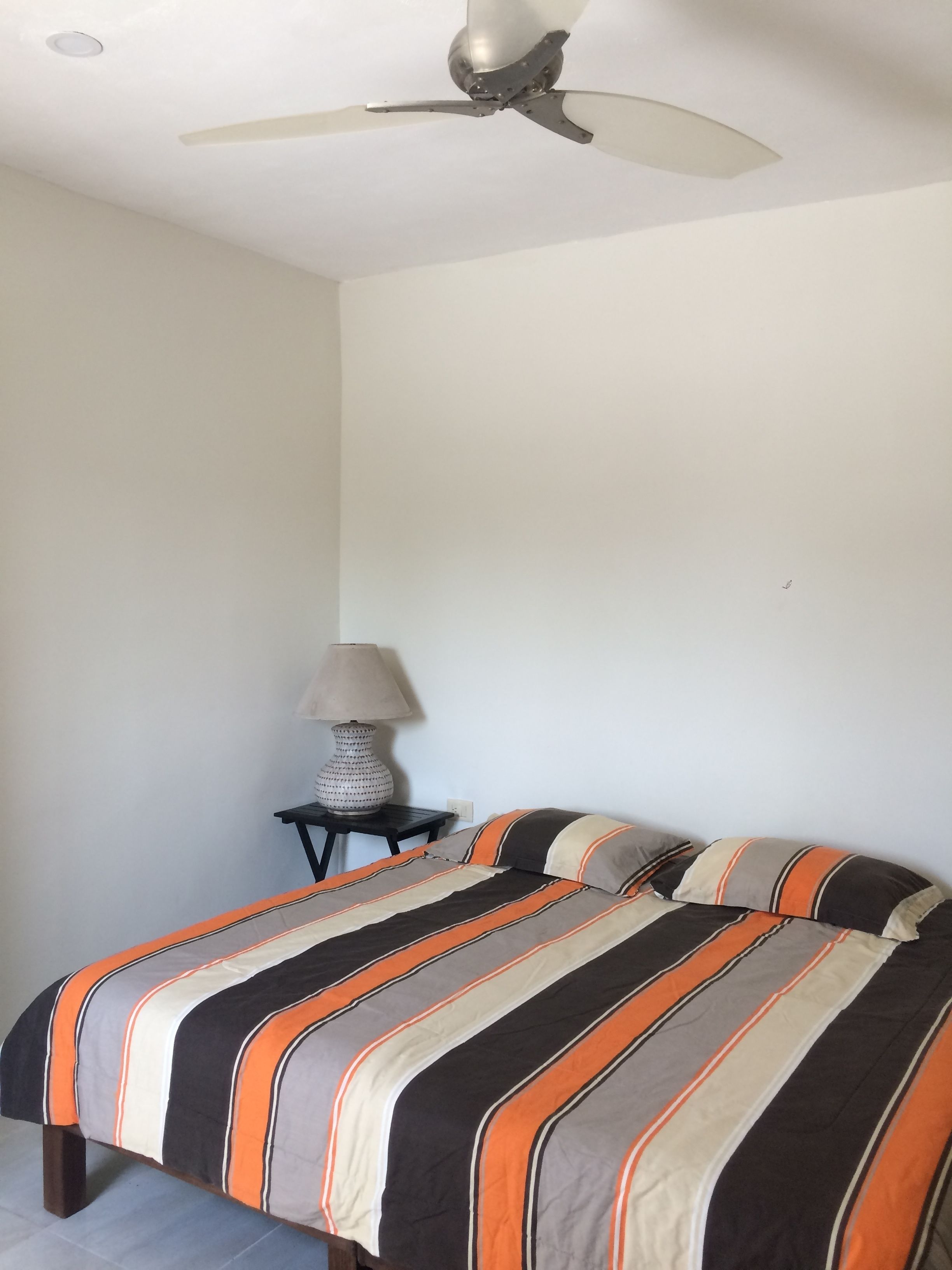 A bedroom with a bed, a ceiling fan, a nightstand, and a lamp.