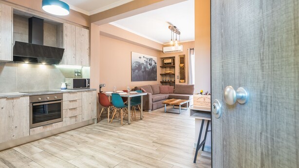 A modern kitchen with a dining area, wooden flooring, and a view into the living room. - Stylish Luxury Apartment near Acropolis at Neos Kosmos metro station  (Neos kosmos)