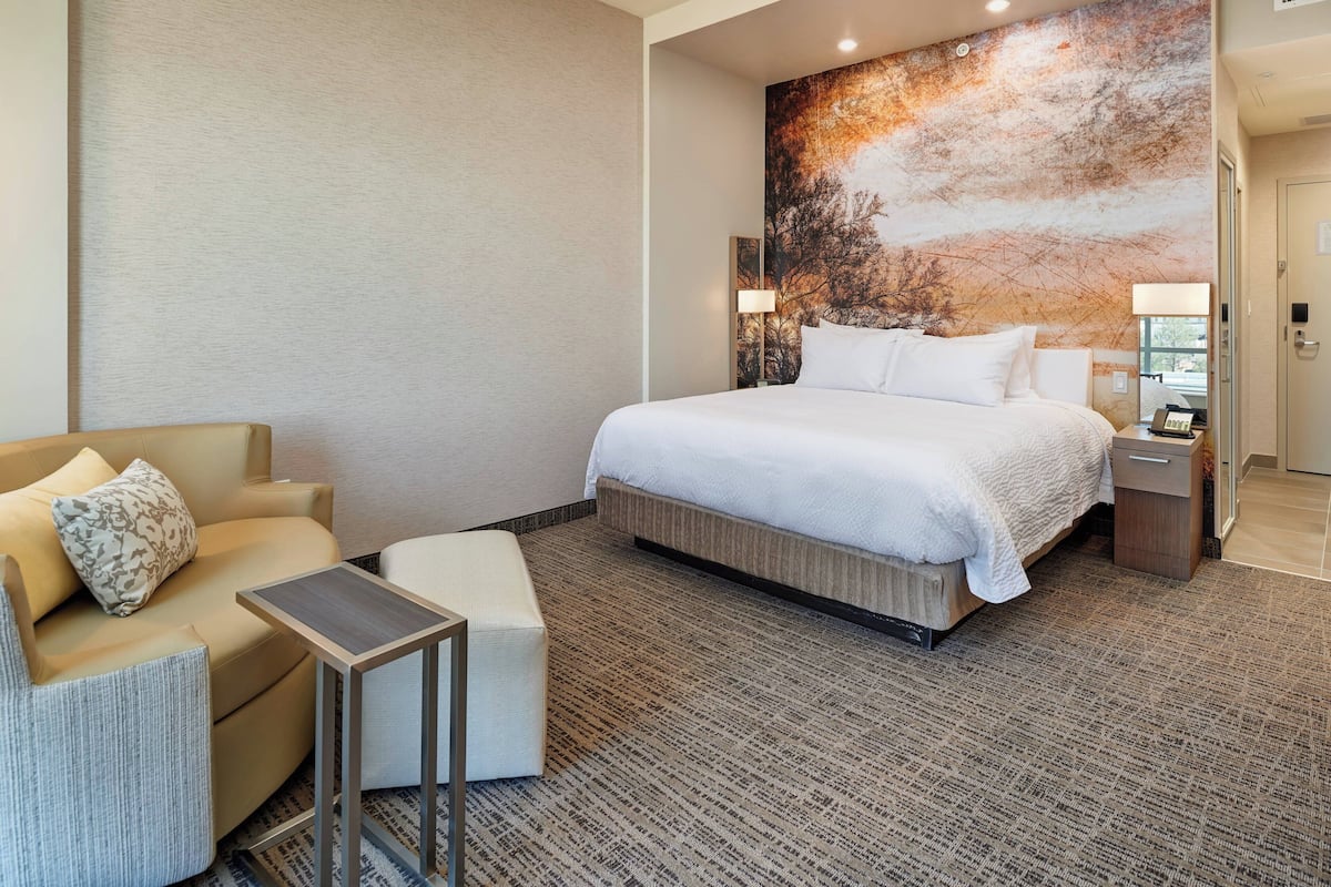 Ein Hotelzimmer mit einem großen Bett, einem Sofa, einem kleinen Tisch und einer Wand mit einem Wandgemälde zum Thema Natur.