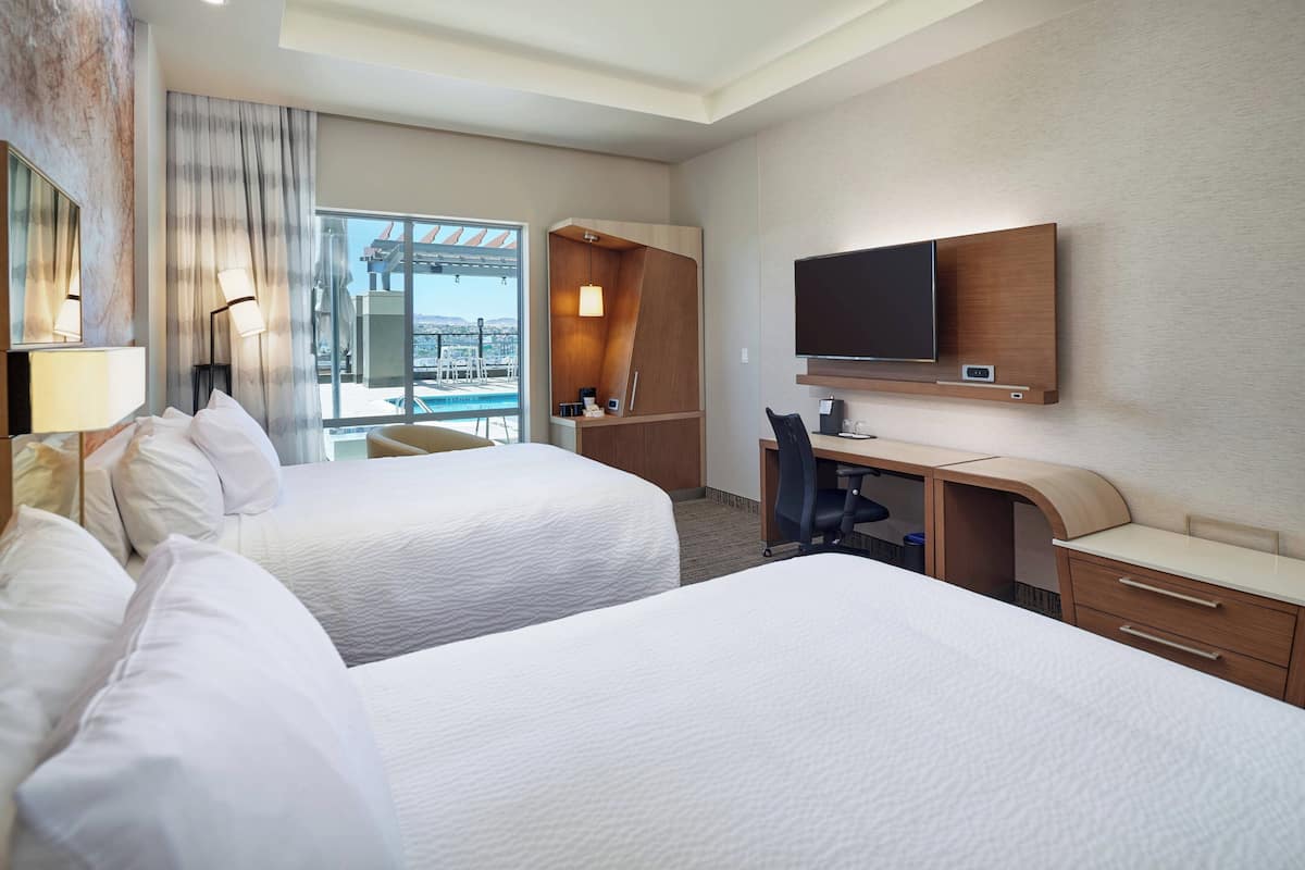 Ein Hotelzimmer mit zwei Betten, einem Schreibtisch, einem Fernseher und Blick auf die Stadt.