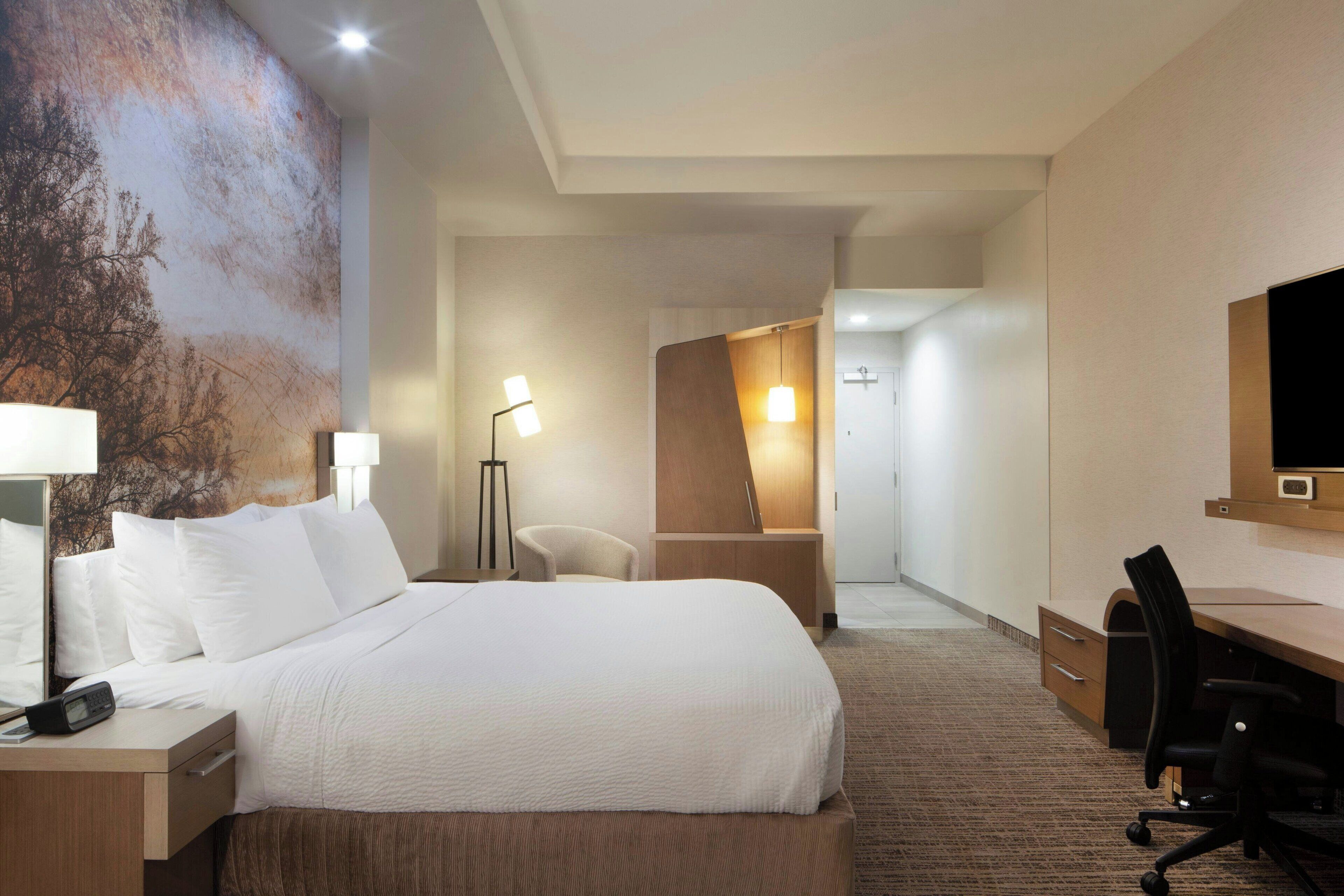 A hotel room with a large bed, a desk with a chair, a flat-screen TV, and a large wall mural.
