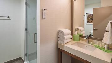 Un baño moderno con cabina de ducha de vidrio, lavabo con artículos de aseo y espejo.