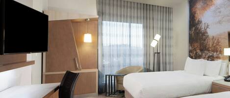 A hotel room with a bed, a desk, a chair, a TV, and a large window with curtains.