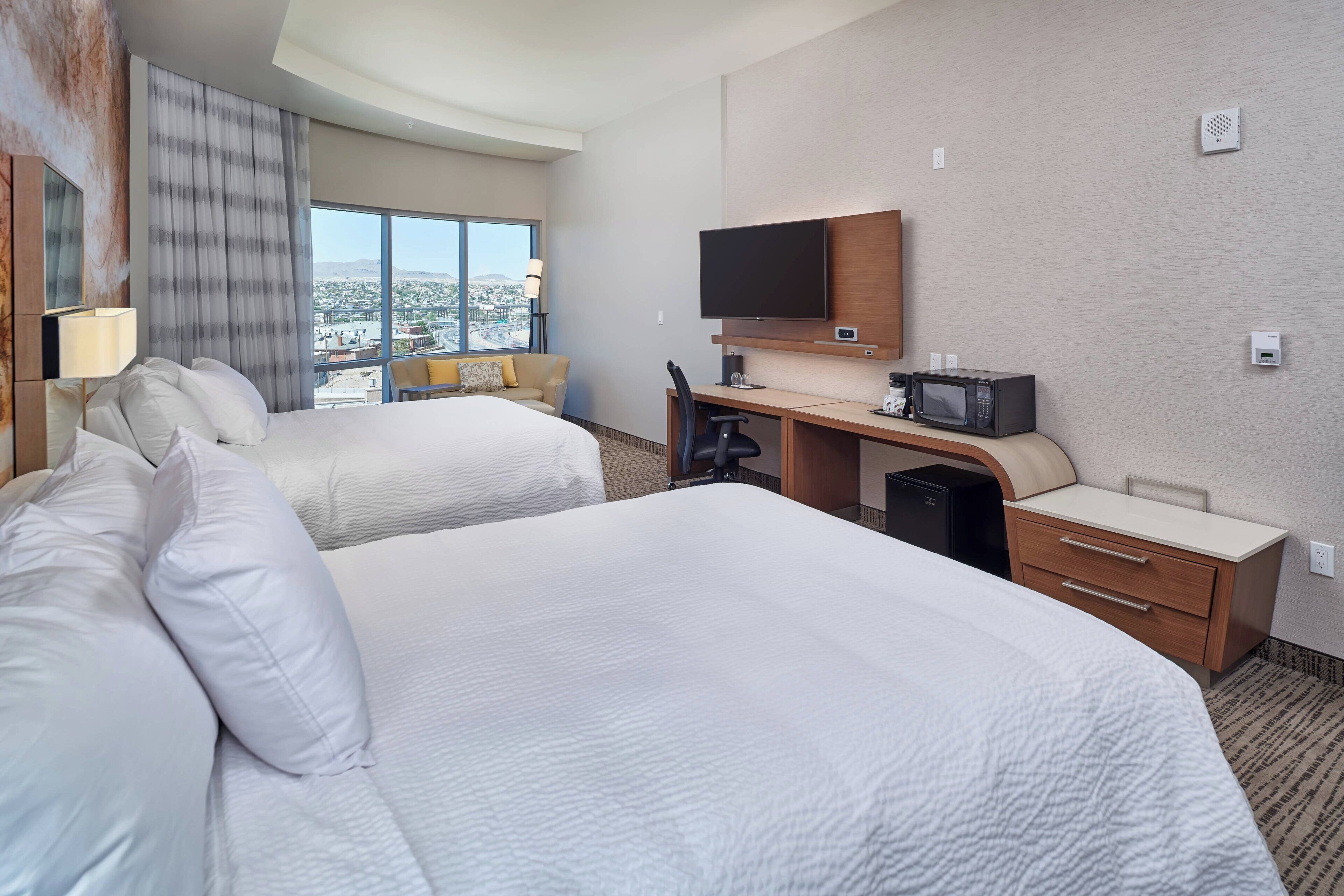 Une chambre d’hôtel avec deux lits, un bureau avec une télévision, une chaise et une vue sur la ville.