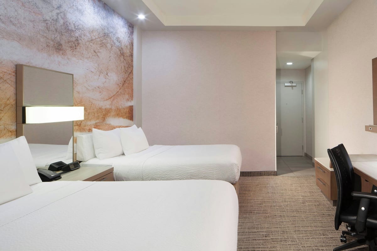 Ein Hotelzimmer mit zwei Betten, einem Schreibtisch, einem Stuhl, einem Telefon und einem Spiegel.
