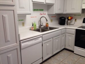 A kitchen with white cabinets, a stainless steel sink, and a dishwasher. There are some items on the counter, including a green bottle and a red bottle. - Los Alamos Flats (Los Alamos)
