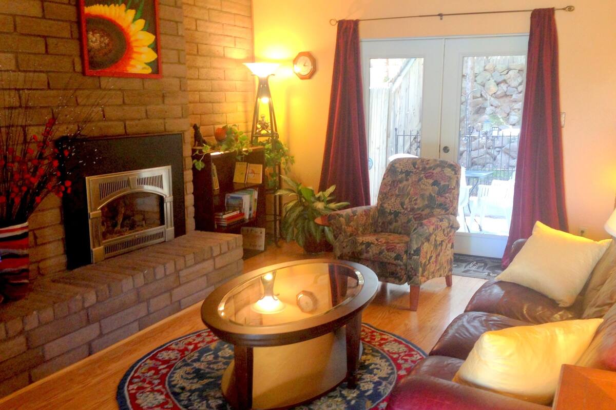 A cozy living room with a fireplace, a floral armchair, a sofa, and a round coffee table.