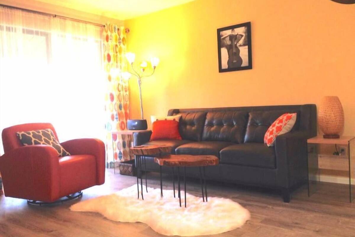 A living room with a black leather sofa, a red armchair, a white furry rug, and a floor lamp.