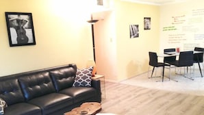 A modern living room with a black leather sofa, a wooden coffee table, and a white furry rug. There is a dining area with a table and chairs in the background. - Los Alamos Flats (Los Alamos)