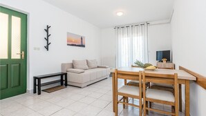 Ein modernes Wohnzimmer mit einer Couch, einem Esstisch mit Stühlen, einem Fernseher und einem Bild an der Wand.