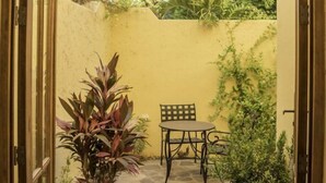 Un chemin de pierre mène à un petit patio agrémenté d’une table et d’une chaise, le tout entouré d’une végétation luxuriante et d’un palmier.