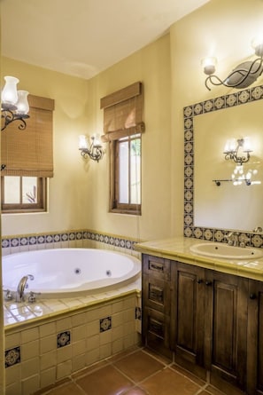 A bathroom with a large bathtub, two sinks, and a mirror with wall sconces.