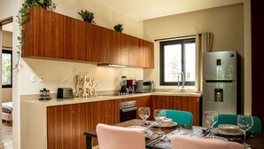 A modern kitchen with wooden cabinets, a built-in island, and a dining area with teal chairs. - Depto en Cancun 506 by Sinbad (Cancun)