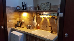 Une petite cuisine équipée d’un évier, d’une bouilloire et de diverses bouteilles.