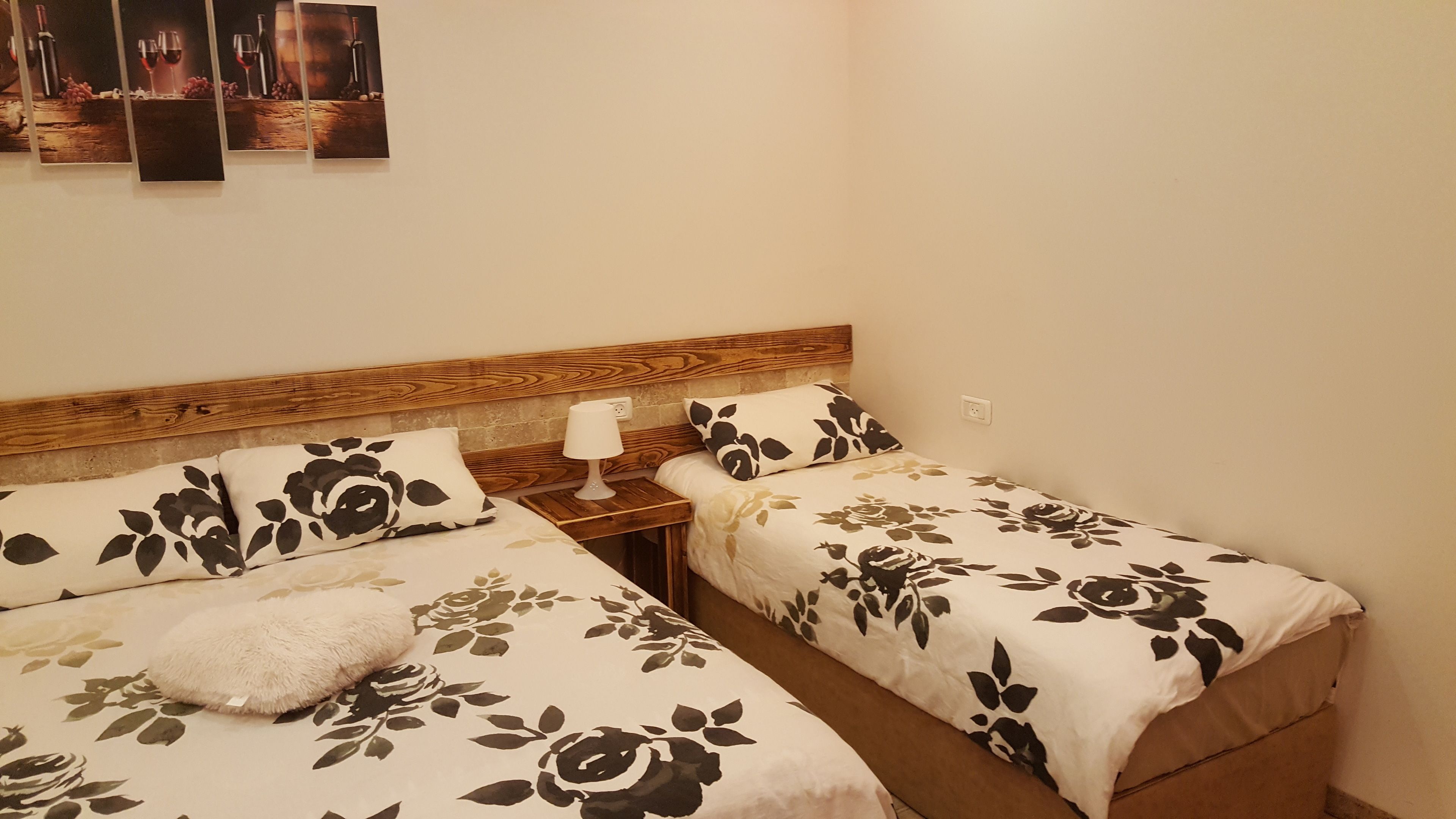 A twin room with two beds, each with floral bedding and a wooden headboard. There is a nightstand with a lamp and a power outlet on the wall.