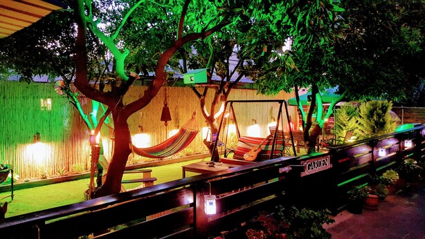 Un espace extérieur aménagé avec des hamacs et une balançoire, entouré d’arbres et délimité par un mur en bambou.