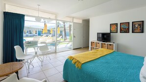 Ett hotellrum med en säng, en tv, en balkong med stolar och ett bord samt utsikt över omgivningarna.