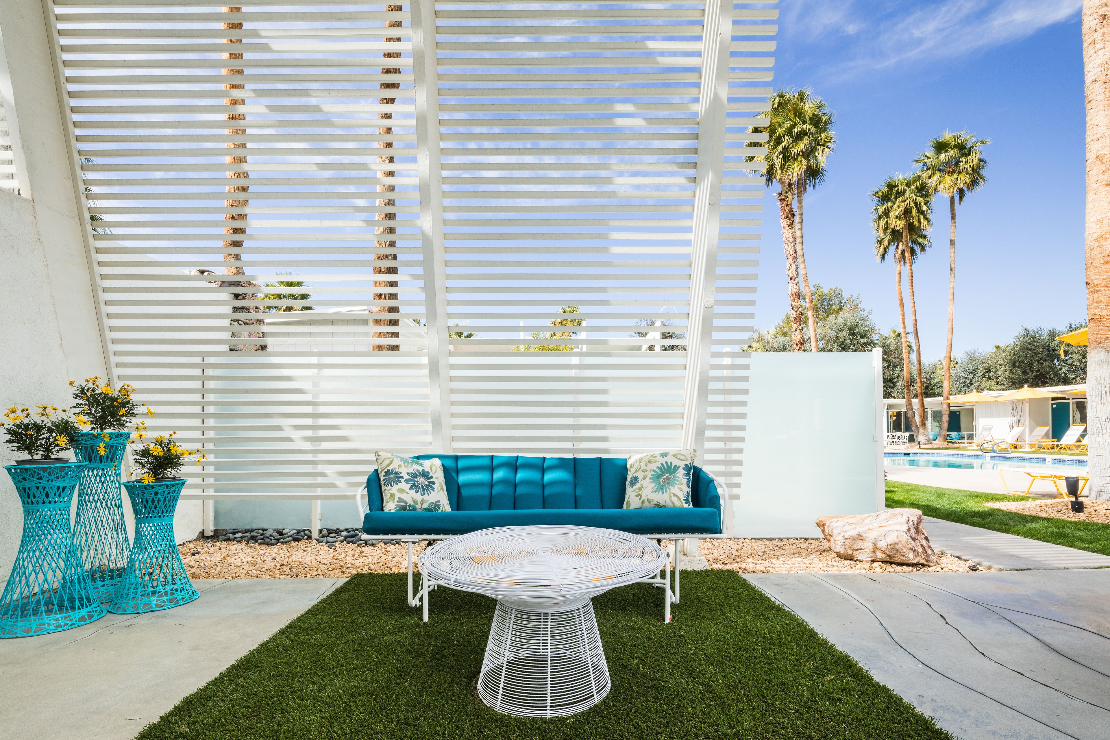Un espace patio comprenant une table en métal blanc, un canapé bleu avec des coussins et des jardinières décoratives.